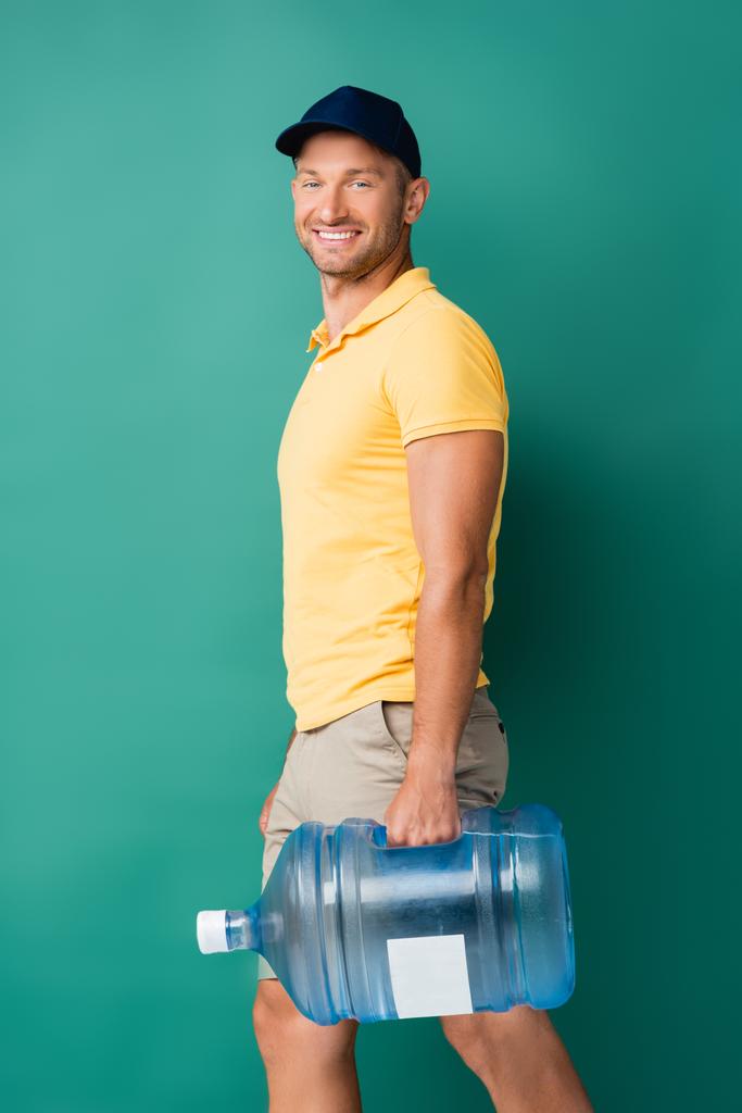 hymyilevä toimitusmies korkissa kantaen vesipulloa sinisellä - Valokuva, kuva