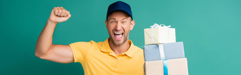 podekscytowany dostawca w czapce trzymając pakowane prezenty na niebiesko, sztandar - Zdjęcie, obraz