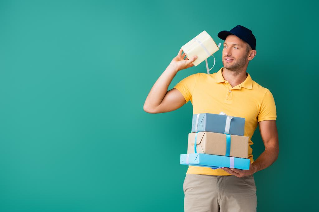 Üniformalı teslimatçı ve şapkalı adam mavi üzerine paketlenmiş hediyeler taşıyor. - Fotoğraf, Görsel
