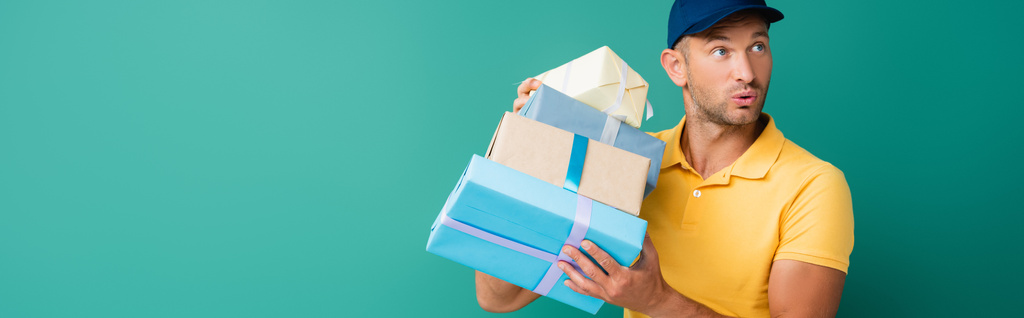 Neugieriger Zusteller in Mütze mit verpackten Geschenken auf blauem Banner - Foto, Bild