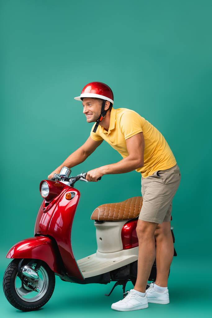 счастливый роженица в шлеме стоит возле красного скутера на синем - Фото, изображение