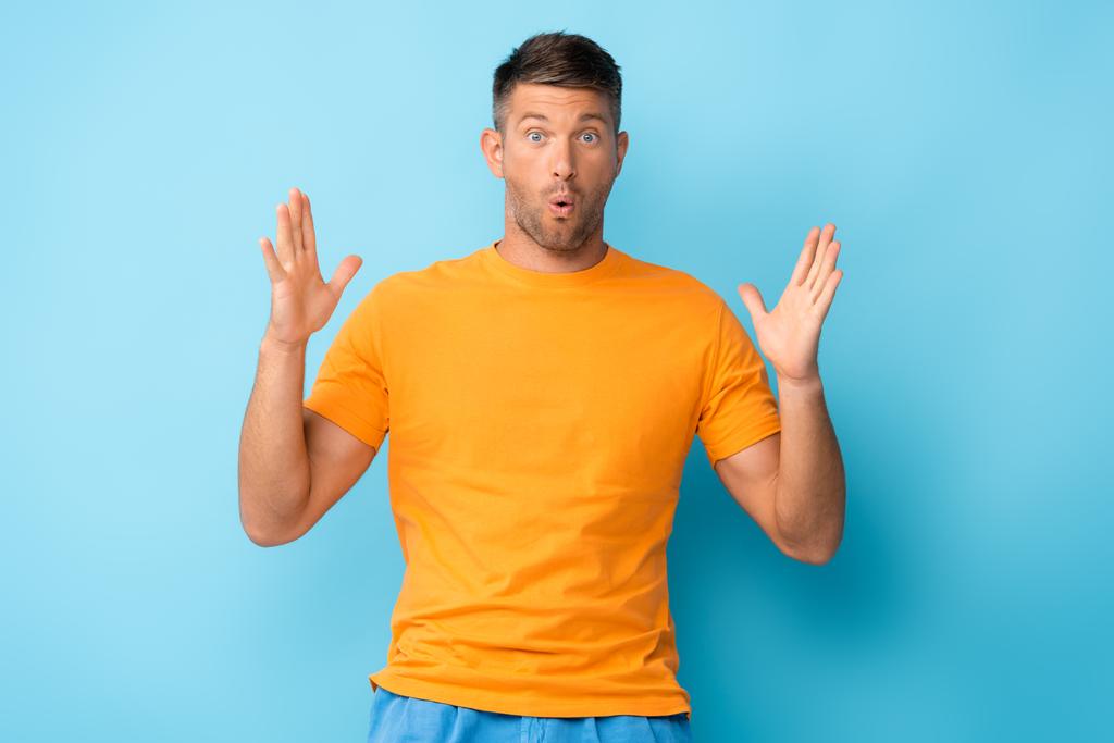 homem surpreso em amarelo t-shirt gesticulando em azul - Foto, Imagem