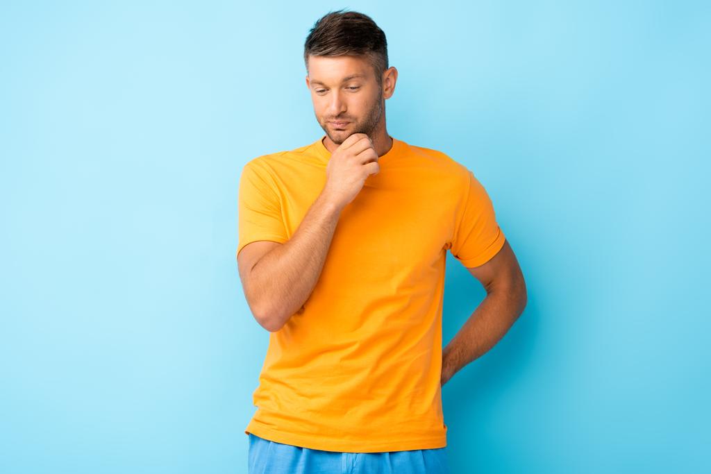 troskliwy mężczyzna w żółtej koszulce spoglądający w dół na niebieski - Zdjęcie, obraz