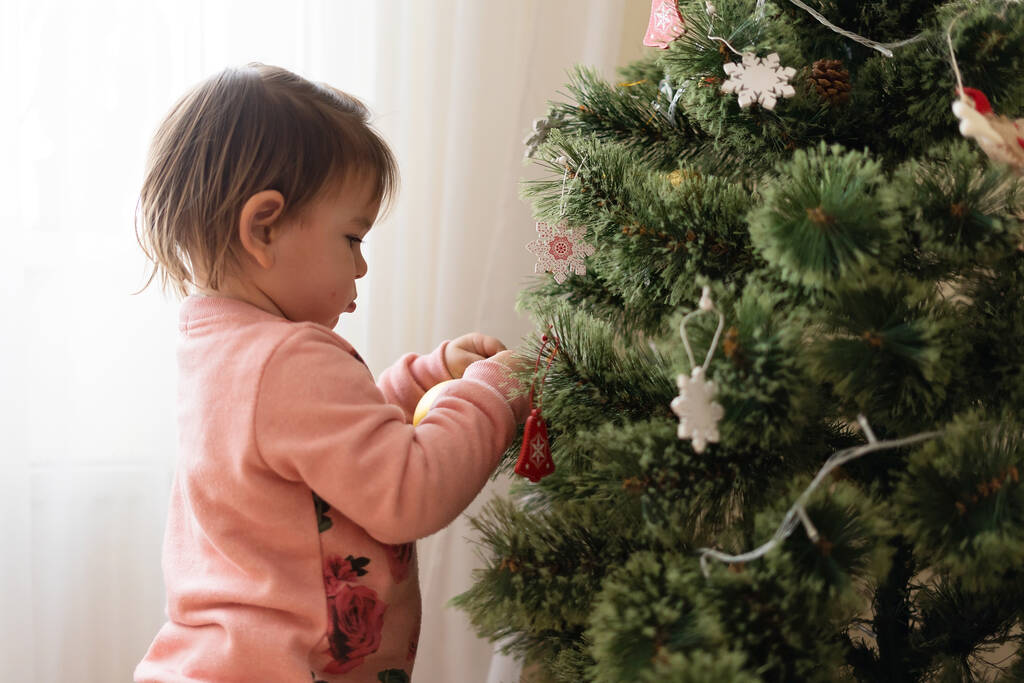 自宅でクリスマスツリーを飾る幼児の女の子。子供のための12月の伝統. - 写真・画像
