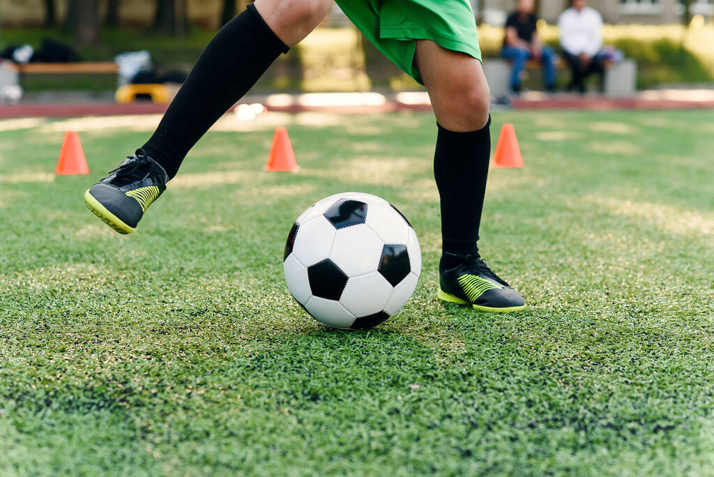 Упорный футболист-подросток, пинающий мяч на поле. Ноги футболиста, пинающего мяч по зеленой траве. - Фото, изображение