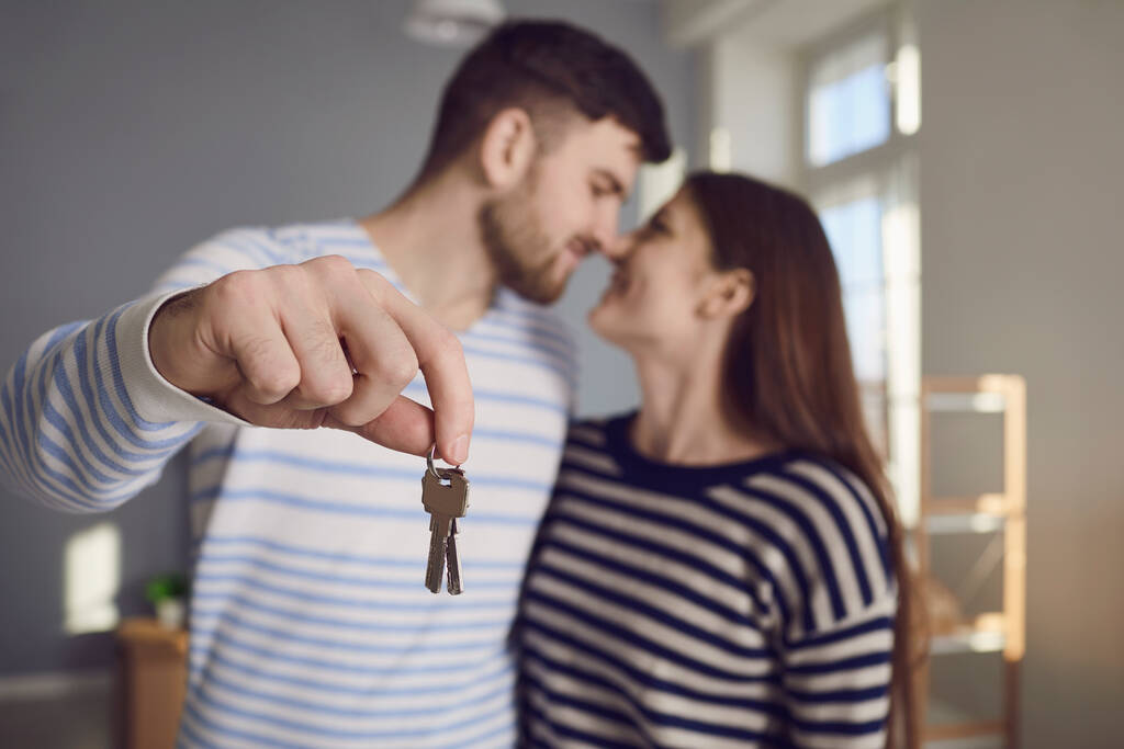 Boldog pár kulcsokkal új otthon a kezében mosolyogva, miközben áll a szobában. - Fotó, kép