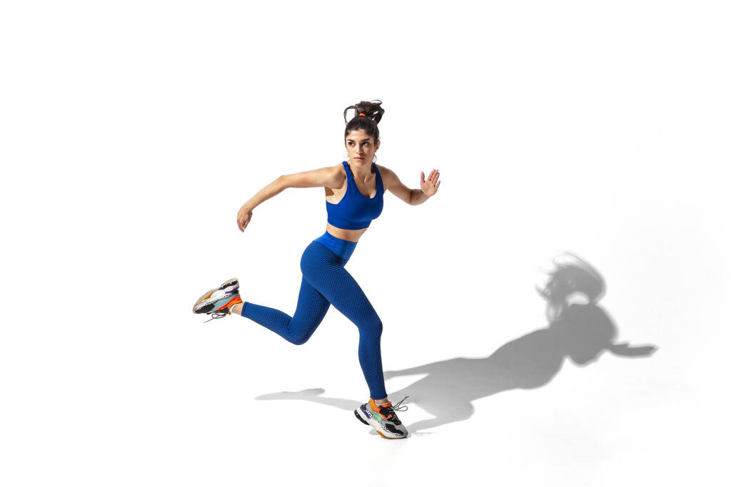 Schöne junge Sportlerin übt auf weißem Studiohintergrund mit Schatten - Foto, Bild
