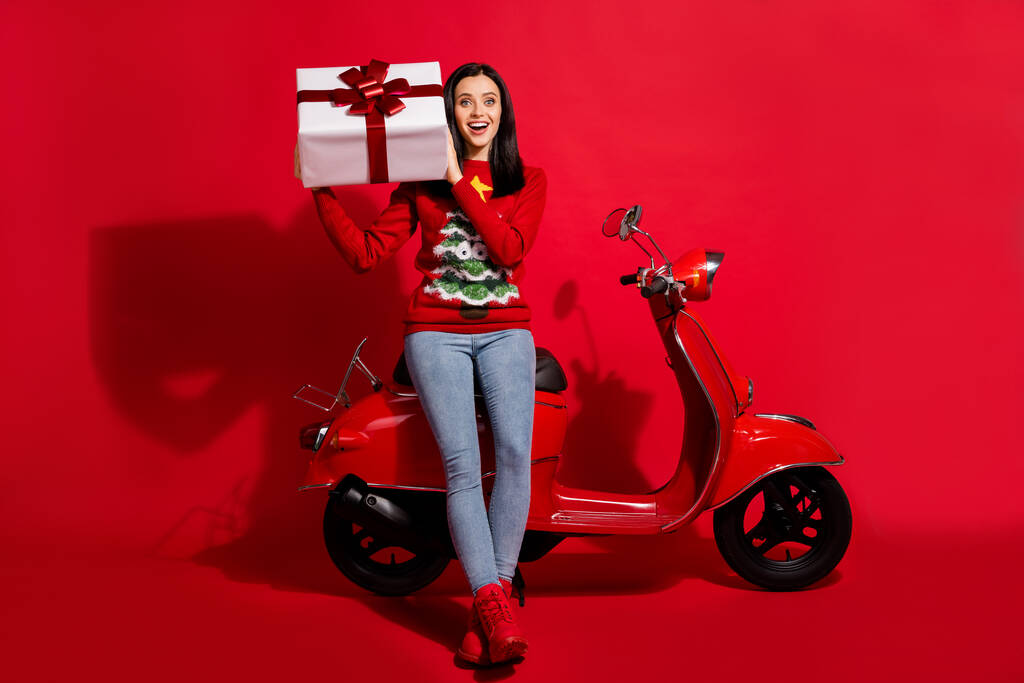 Full length body size view of her she nice attractive glad cheerful girl sitting on moped holding in hand big giftbox st nicholas day isolated bright vivid shine vibrant red color background - Фото, изображение