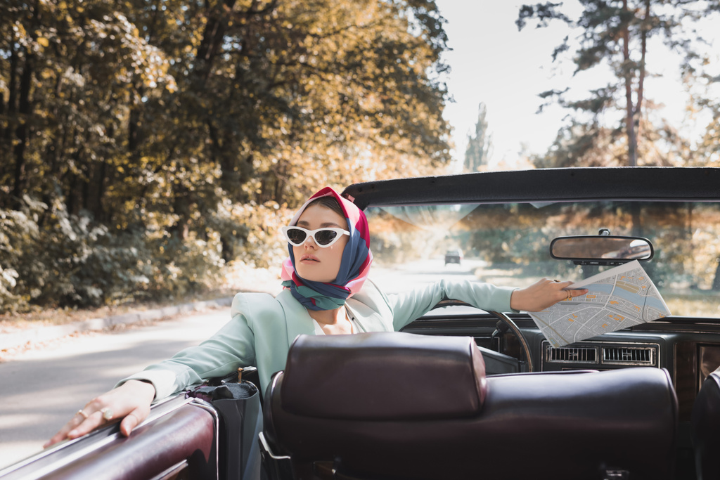 Tyylikäs nainen, jolla on kartta istuu kuljettajan istuimella kattoman auto hämärtynyt etualalla - Valokuva, kuva