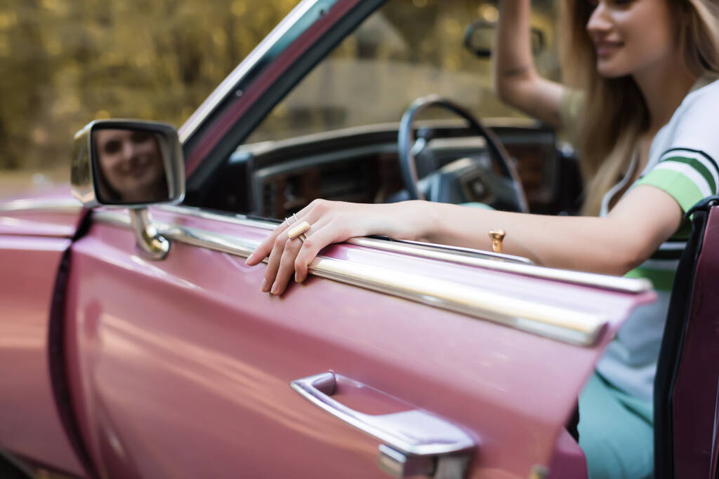 vista recortada de la mujer abriendo la puerta de cabriolet mientras mira en el espejo de vista lateral sobre fondo borroso - Foto, Imagen