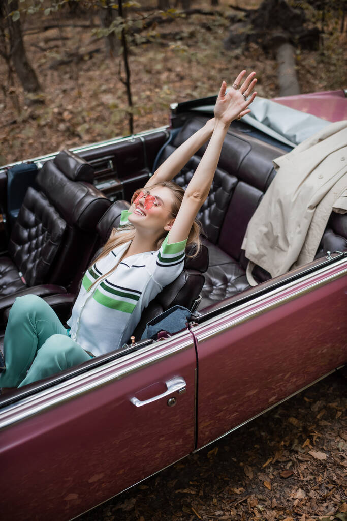 vue grand angle de femme joyeuse se détendre tout en étant assis dans le cabriolet rétro et les mains tendues - Photo, image