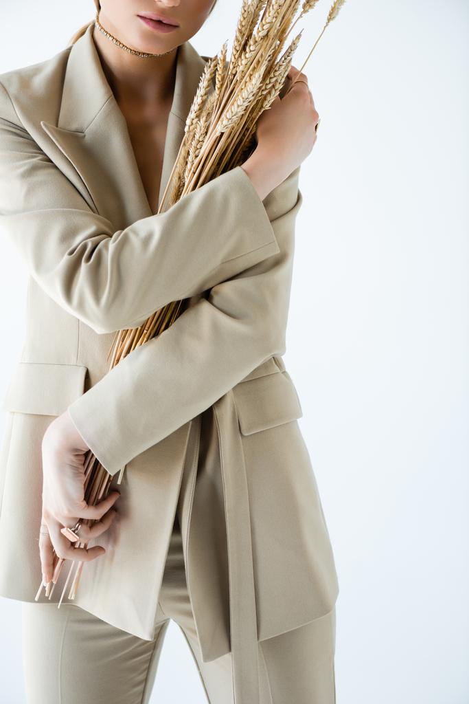 vista cortada de mulher jovem em blazer bege segurando trigo no branco - Foto, Imagem