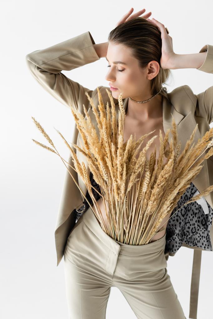 стильная модель в бежевой формальной одежде с шипами пшеницы позирует изолированно на белом  - Фото, изображение