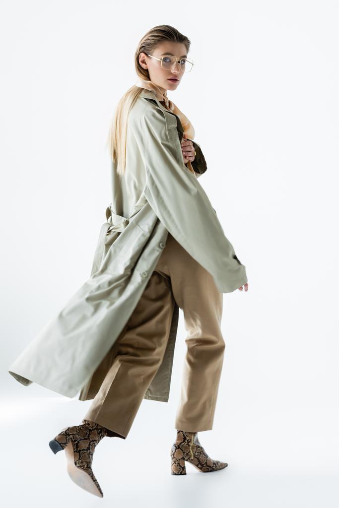full length of stylish woman in glasses, trench coat and scarf walking on white - Photo, Image