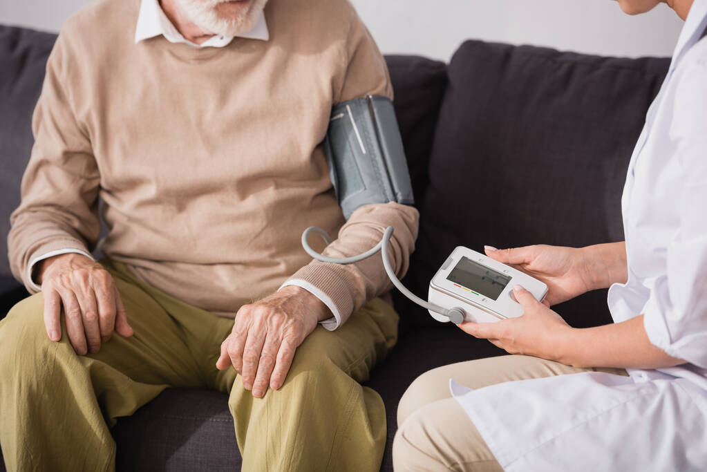 bijgesneden weergave van geriatrische verpleegkundige onderzoeken oudere man met tonometer thuis - Foto, afbeelding