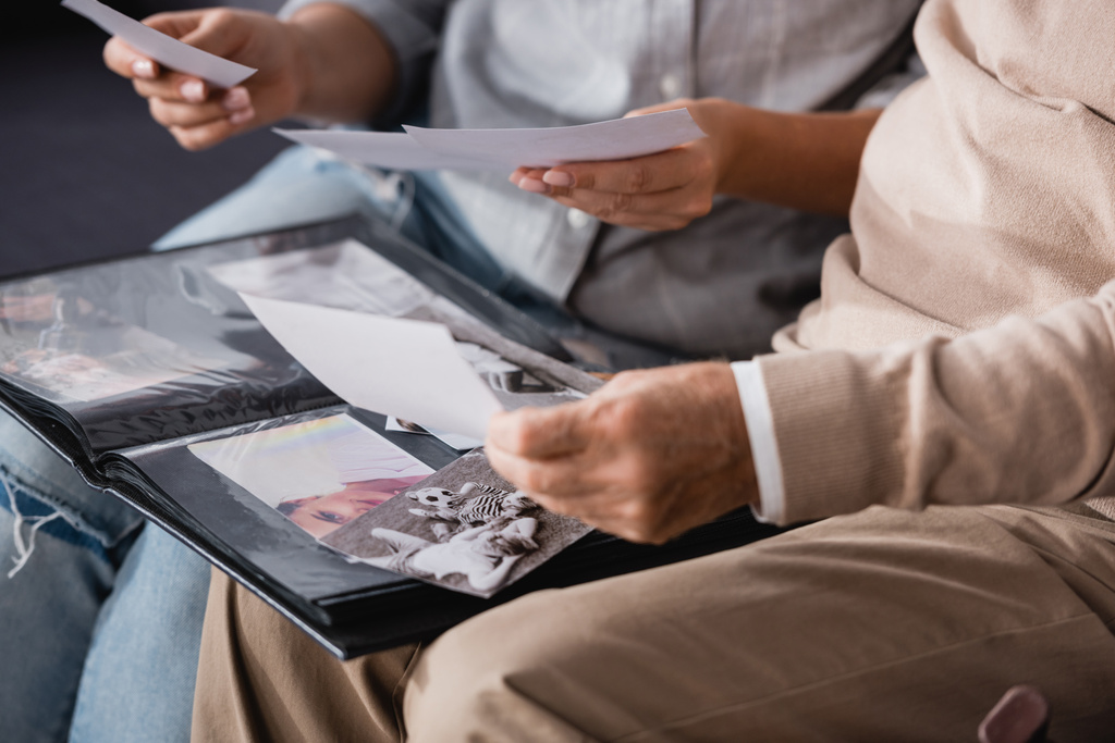 cropped view of aged father and adult daughter looking at family photos together on blurred background - Photo, Image