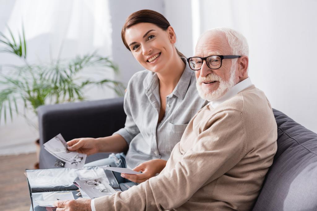smiling woman with elderly father looking at camera while looking at family photos together - Photo, Image
