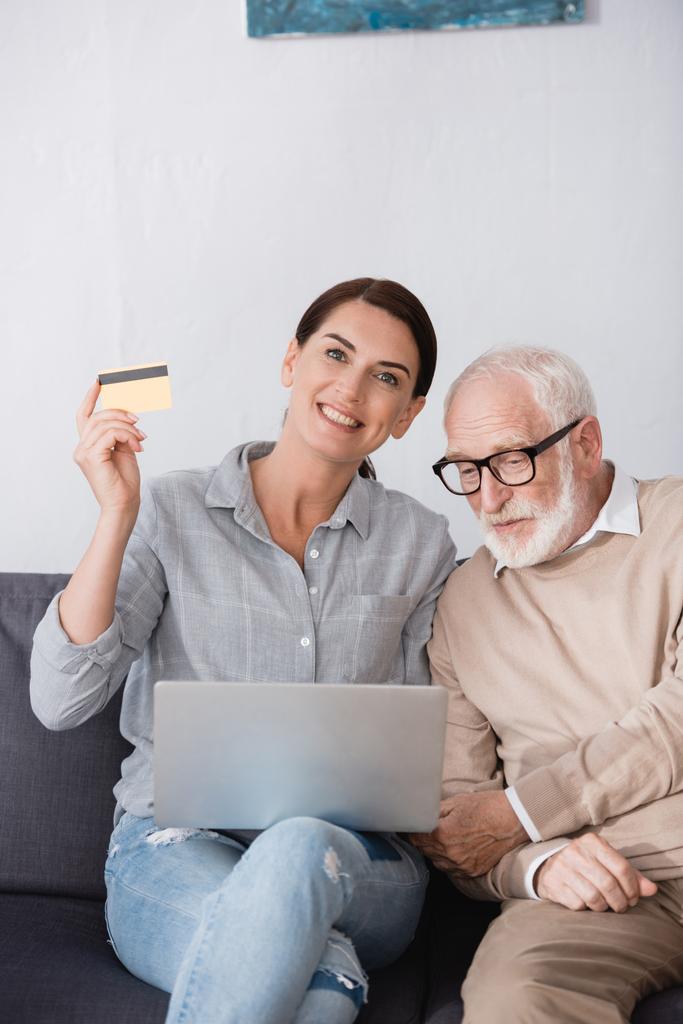 vidám nő kezében laptop és hitelkártya, miközben ül mellett idős apa - Fotó, kép