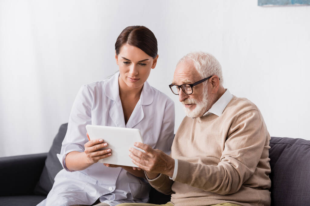 Esmer yaşlı hemşire ve yaşlı adam dijital tablet kullanıyorlar. - Fotoğraf, Görsel