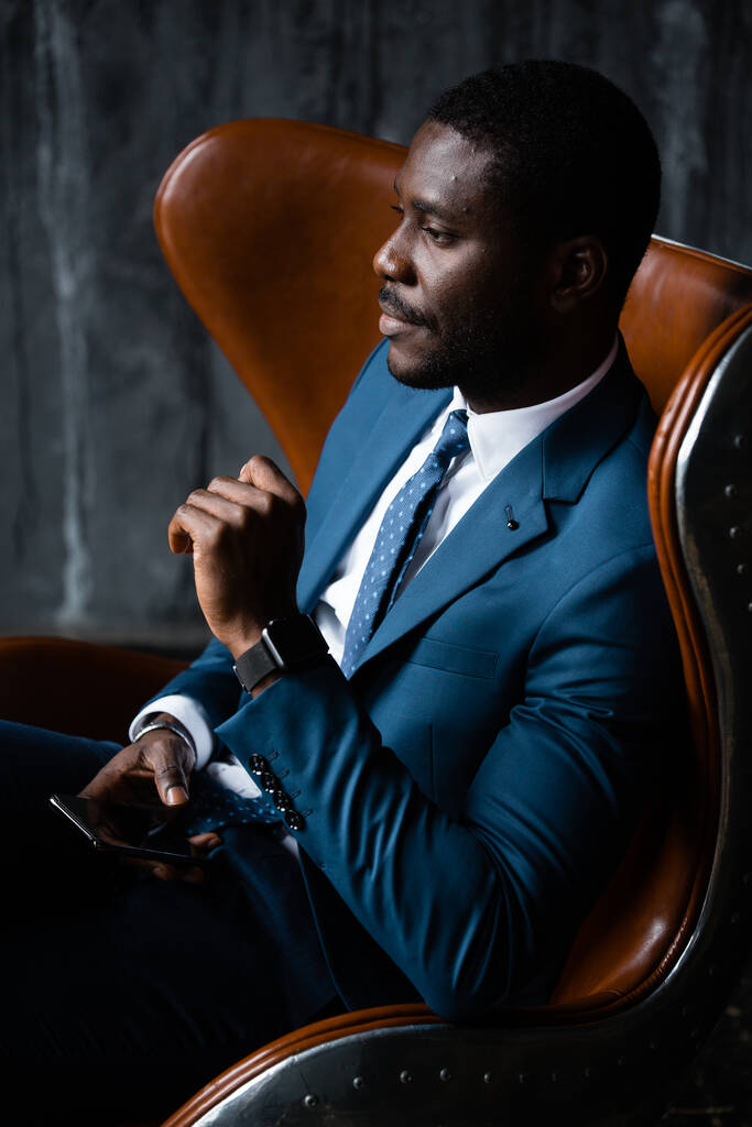 Homme d'affaires afro-américain assis dans un fauteuil loft avec un téléphone dans ses mains - Photo, image