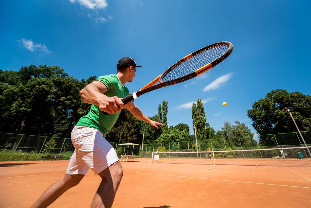 Νεαρός αθλητικός άνδρας που παίζει τένις στο γήπεδο. - Φωτογραφία, εικόνα