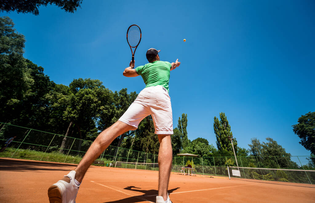 Νεαρός αθλητικός άνδρας που παίζει τένις στο γήπεδο. - Φωτογραφία, εικόνα