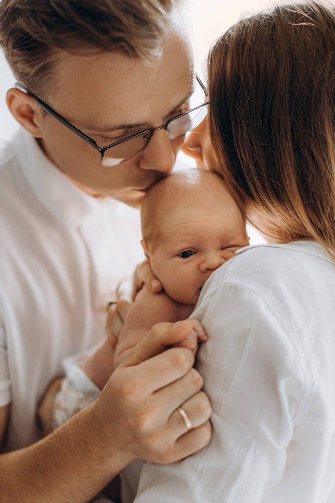 Piękna rodzina z noworodka, kochająca mama trzymać małą córkę w ramionach, opiekuńczy tata delikatnie pocałować uroczą dziewczynkę, trzymać jej malutką rączkę, cieszyć się delikatnymi chwilami, rodzicielskie pojęcie - Zdjęcie, obraz