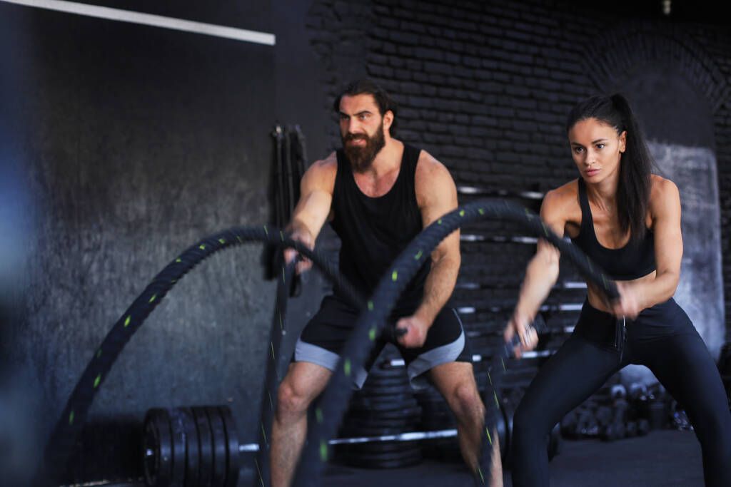 Αθλητικό νεαρό ζευγάρι με σχοινί μάχης κάνει άσκηση σε λειτουργική προπόνηση γυμναστήριο φυσικής κατάστασης - Φωτογραφία, εικόνα
