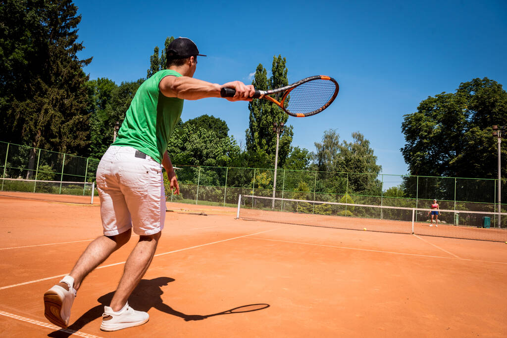 Mladý atletický muž hraje tenis na hřišti. - Fotografie, Obrázek