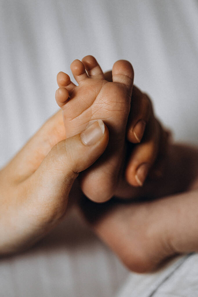 Porträt von entzückenden Beinchen mit winzigen Fingern, von entzückenden neugeborenen Mädchen, in fürsorglichen Armen der Eltern, glücklichen Familienmomenten, Geburt und Kindheitskonzept - Foto, Bild