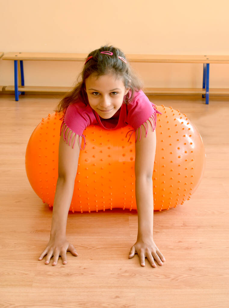 Bir kız spor salonunda büyük bir jimnastik topunun üzerinde yatıyor. - Fotoğraf, Görsel