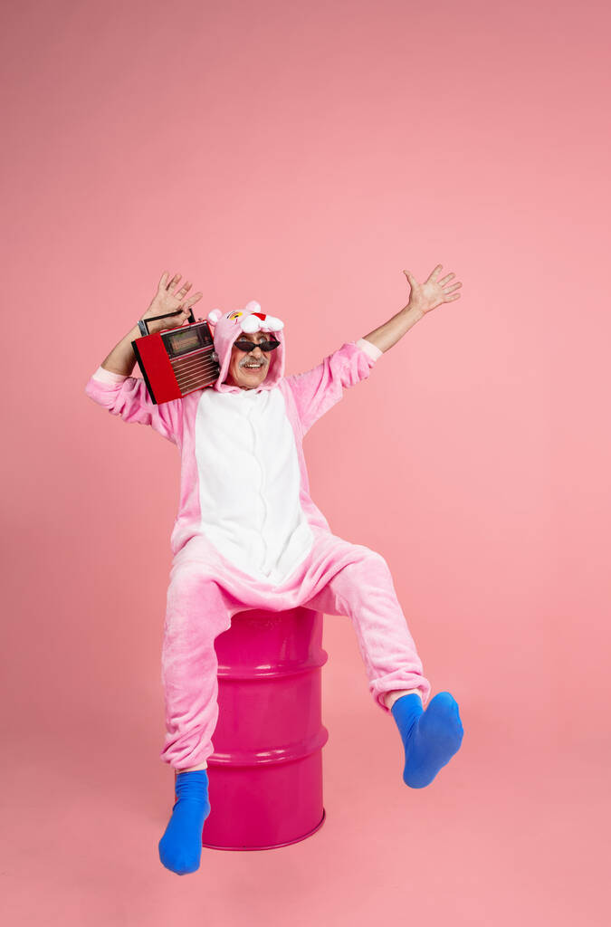 Старший хипстер мужчина в стильной розовой одежде изолирован на розовом фоне. Технология и радостный образ жизни пожилых людей - Фото, изображение