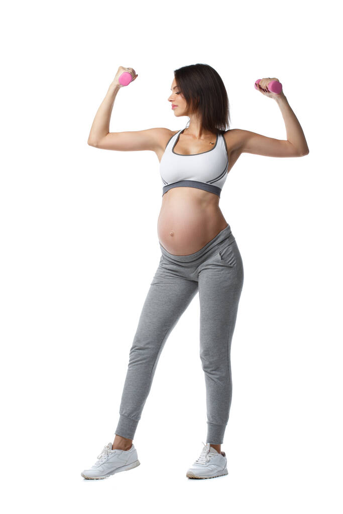 mince athlétique enceinte fille est engagée dans remise en forme avec haltères debout en pleine longueur isolé sur fond blanc. - Photo, image