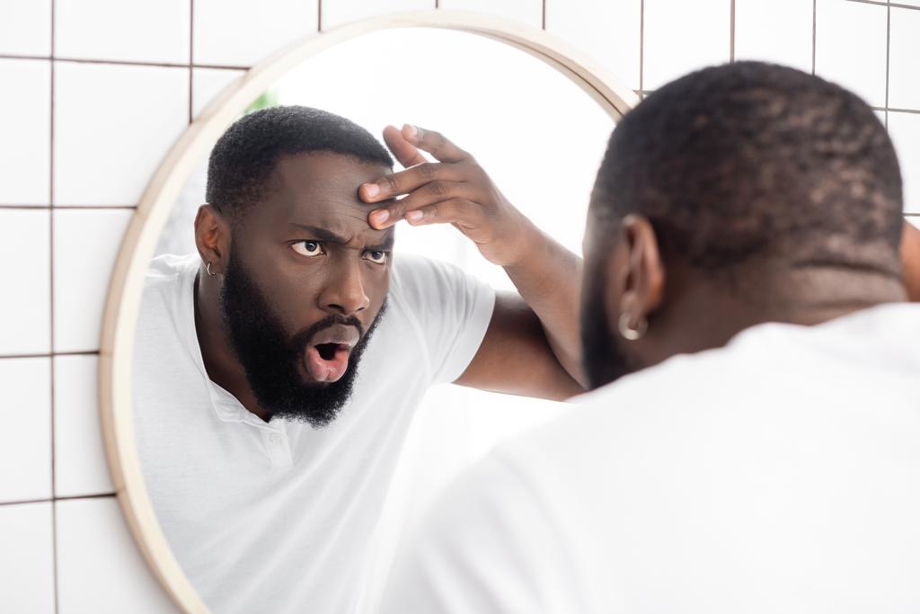 σοκαρισμένος αφρο-Αμερικανός άντρας που κοιτάζει ρυτίδες στον καθρέφτη. - Φωτογραφία, εικόνα