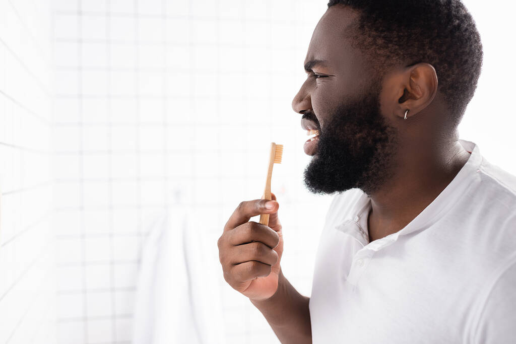 Hoş olmayan Afro-Amerikalı adamın dişlerini fırçalamasının yan görüntüsü - Fotoğraf, Görsel