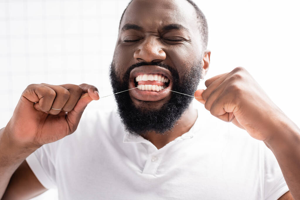 portrét afro-amerického muže se zavřenýma očima za použití zubní nitě - Fotografie, Obrázek