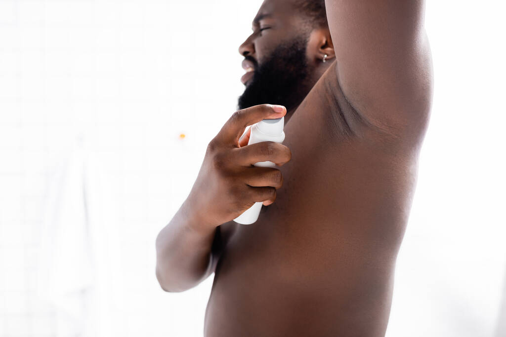 hombre afroamericano con la mano hacia arriba usando desodorante - Foto, Imagen