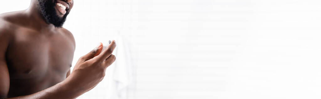 panoramiczne ujęcie uśmiechniętego afro-amerykanina używającego dezodorantu - Zdjęcie, obraz