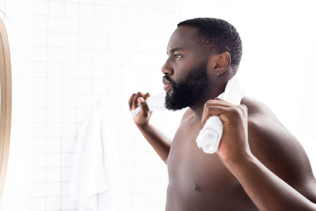 σοβαρός Αφρο-Αμερικανός άντρας κοιτάζεται στον καθρέφτη με πετσέτα πίσω από το λαιμό  - Φωτογραφία, εικόνα