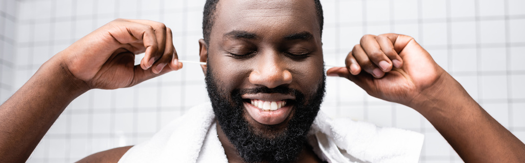 plano panorámico de hombre afro-americano limpiando orejas con orejeras - Foto, imagen