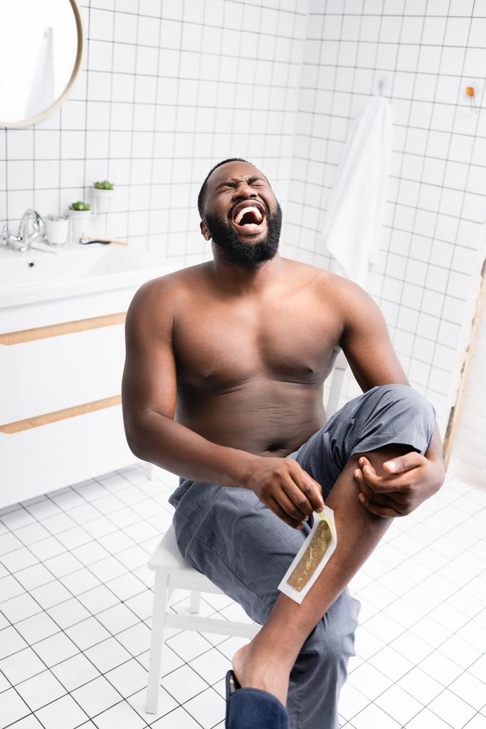 afro-americano homem arrancando tiras de cera e gritando de dor  - Foto, Imagem