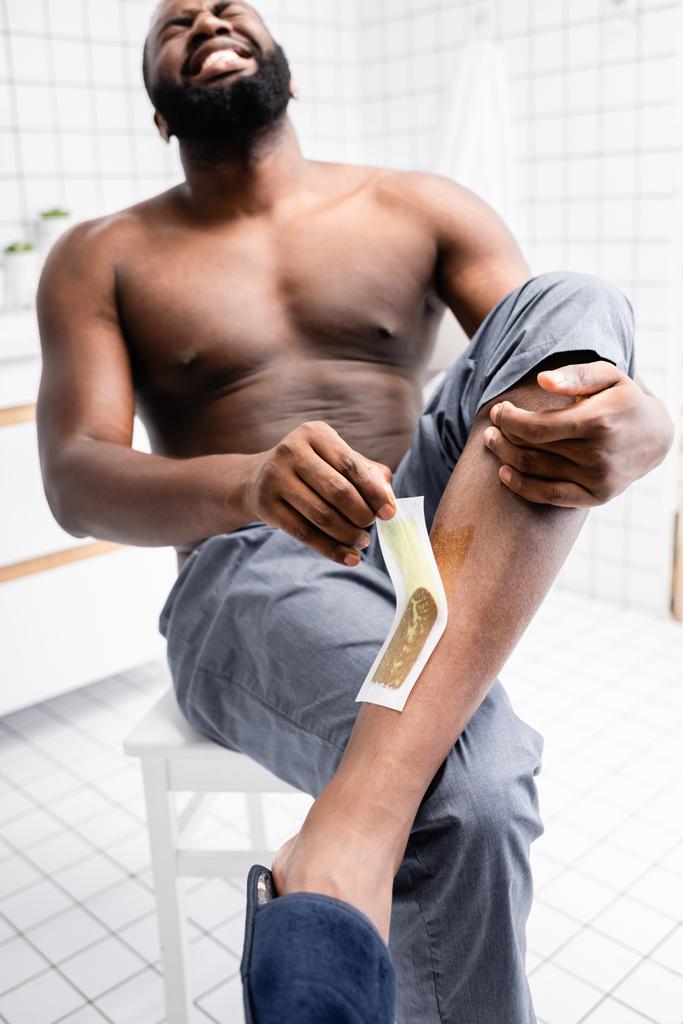 Αφρο-αμερικάνος που σκίζει λωρίδες κεριού και υποφέρει από πόνο.  - Φωτογραφία, εικόνα