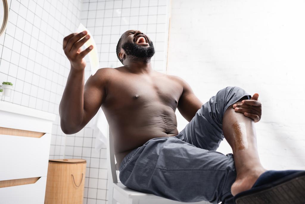 hombre afroamericano arrancando tiras de cera y gritando de dolor  - Foto, Imagen