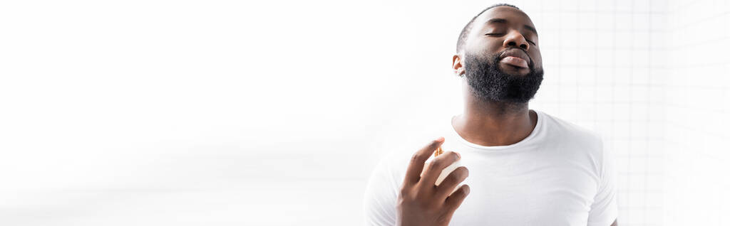 panoraama laukaus afroamerikkalainen mies valkoinen t-paita käyttäen hajuvettä - Valokuva, kuva