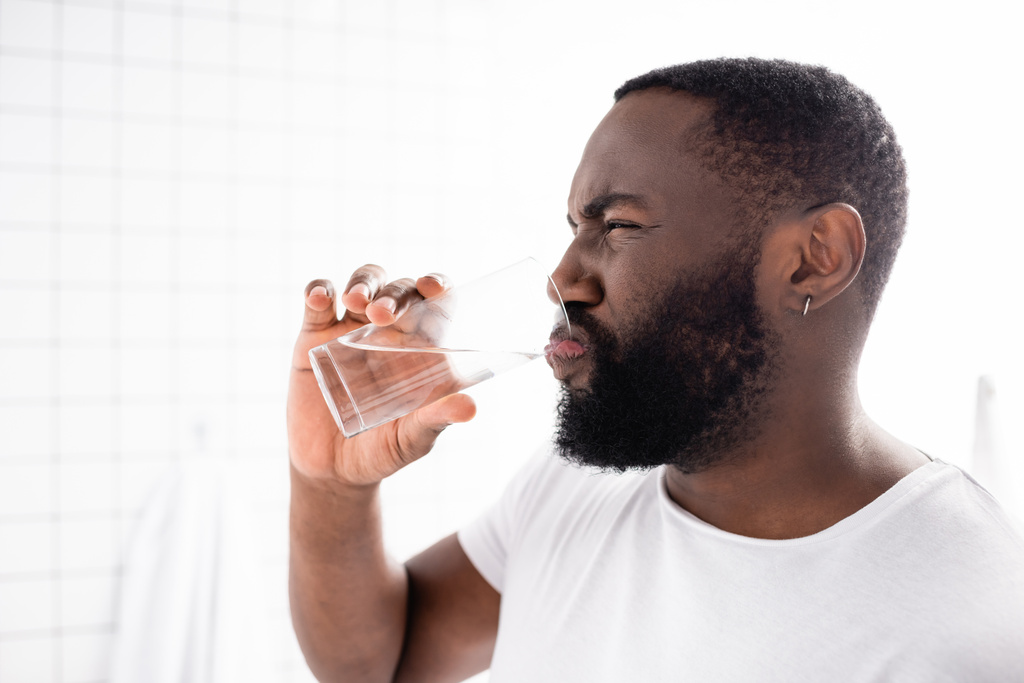 Afrikaans-Amerikaanse man grimmig en drinkwater - Foto, afbeelding