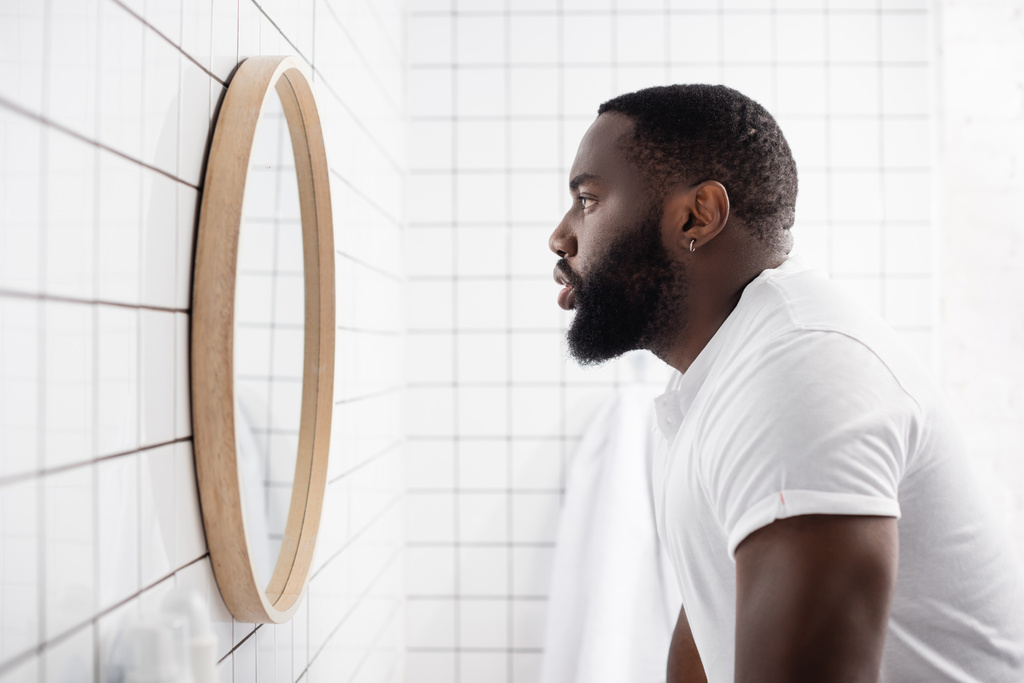 vista lateral del hombre afro-americano serio mirando en el espejo - Foto, Imagen