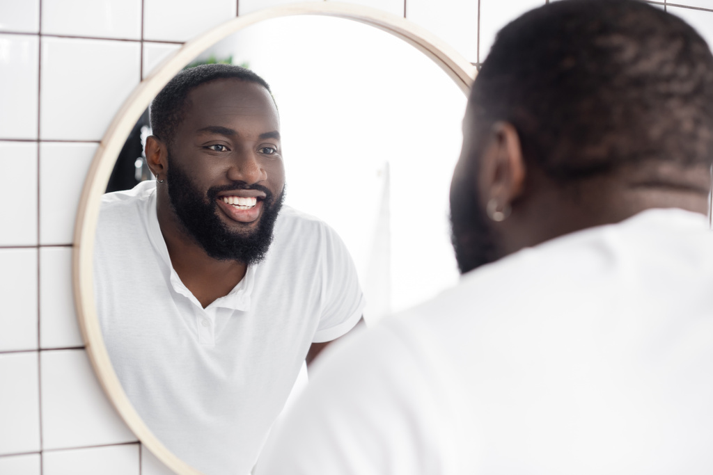 χαμογελαστός Αφρο-Αμερικανός άντρας κοιτάζεται στον καθρέφτη - Φωτογραφία, εικόνα
