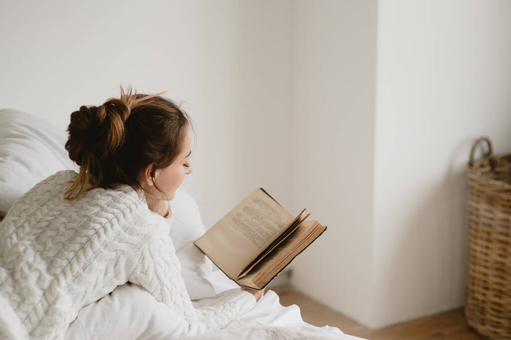 fiatal nő olvasás könyv az ágyban otthon. - Fotó, kép