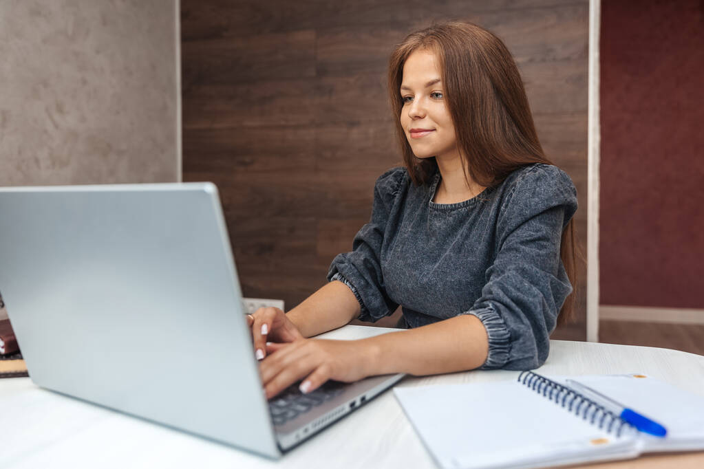 Молода жінка працює на ноутбуці вдома, сидячи за робочим столом
 - Фото, зображення