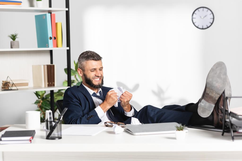 Stressed businessman holding clumped paper near laptop and stationery on blurred foreground  - Photo, Image